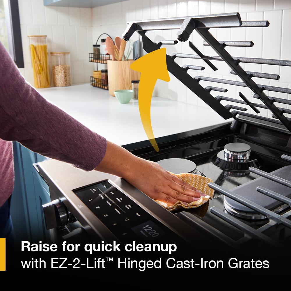 Person lifting hinged cast-iron grate on black gas range cooktop for easy cleaning in modern kitchen setting