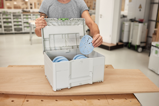 Person placing blue perforated sanding discs into gray Festool abrasives storage Systainer for tool organization