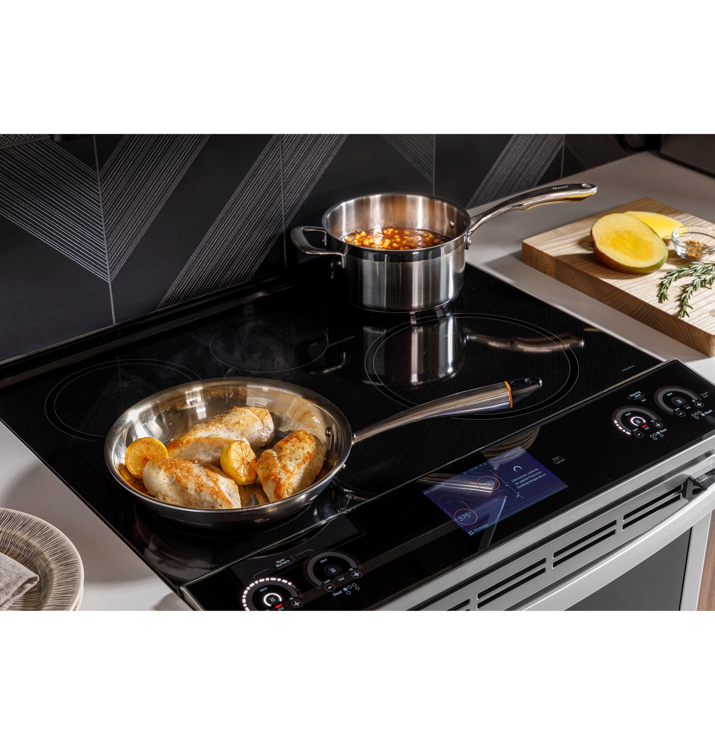 GE Profile induction cooktop with stainless steel pans cooking chicken and sauce, modern range in kitchen setting
