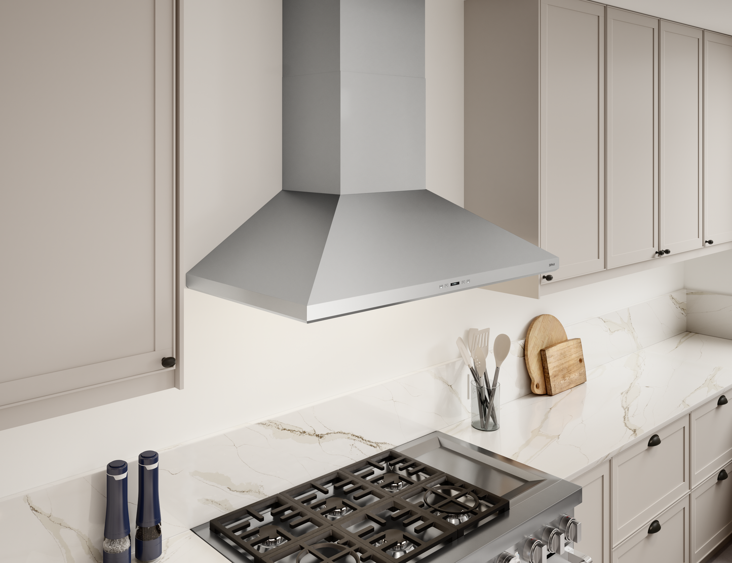 Stainless steel wall mounted range hood above stainless gas cooktop in modern kitchen with beige cabinetry