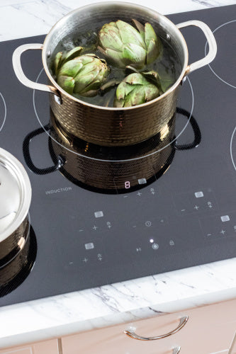 Black induction cooktop with five cooking zones and digital touch controls in a modern kitchen setting