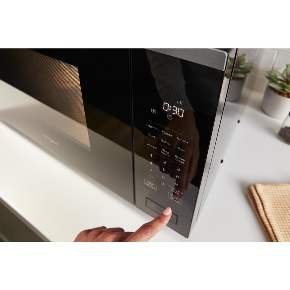 Person pressing start button on black sensor cooking microwave with digital display on white countertop