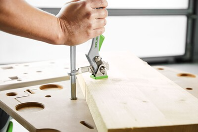 Person securing a wood board on a perforated beige worktable in a woodworking tools and tool stands setting