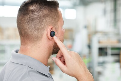 Man adjusting black Bluetooth earplug in ear for noise reduction and safety in a hardware workshop environment