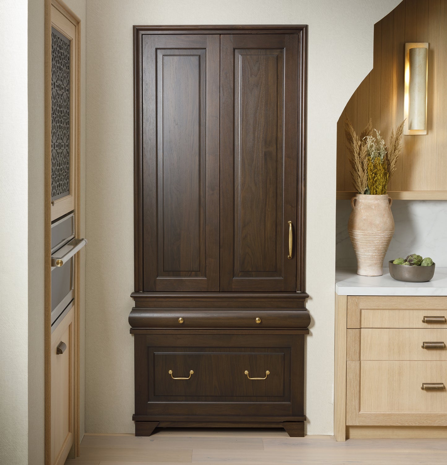Built-in dark wood panel refrigerator integrated into modern kitchen with light wood cabinetry and decorative accents