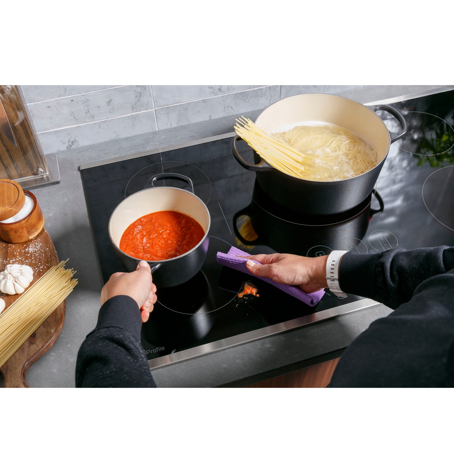 Black built-in induction cooktop with dual pots heating pasta and sauce in a modern kitchen setting