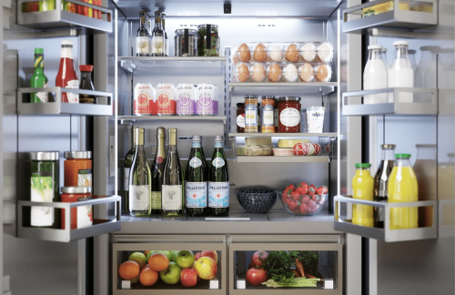 Open built-in French door refrigerator showing organized shelves with beverages, eggs, fruits, and fresh produce inside