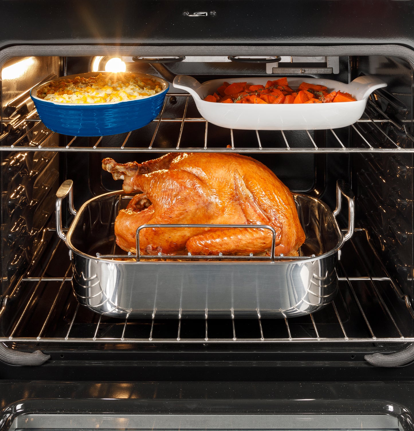Roast turkey cooking inside oven with side dishes of macaroni and cheese and roasted carrots in kitchen range setting