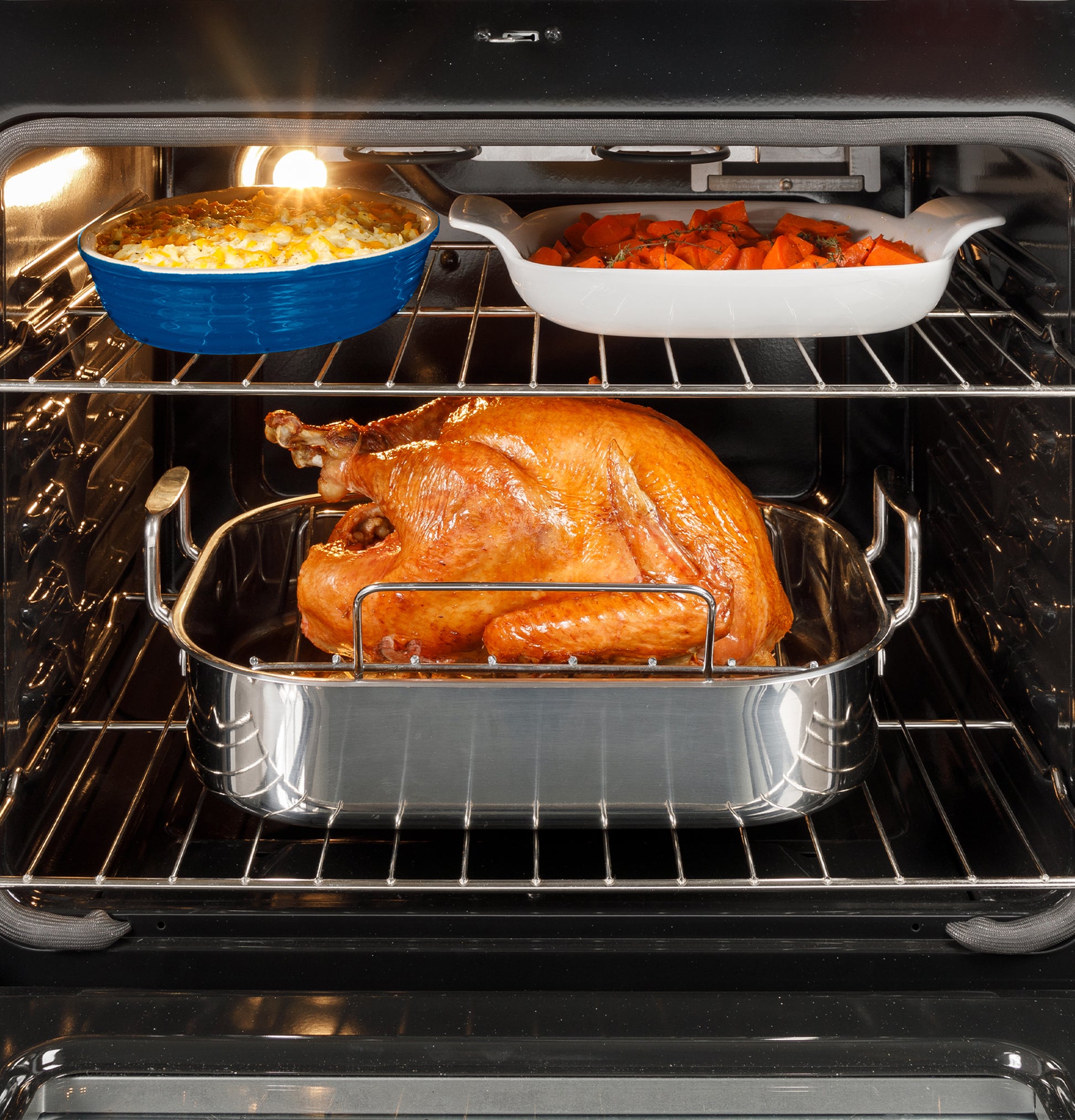 Roast turkey cooking inside oven with side dishes of macaroni and cheese and roasted carrots in kitchen range setting