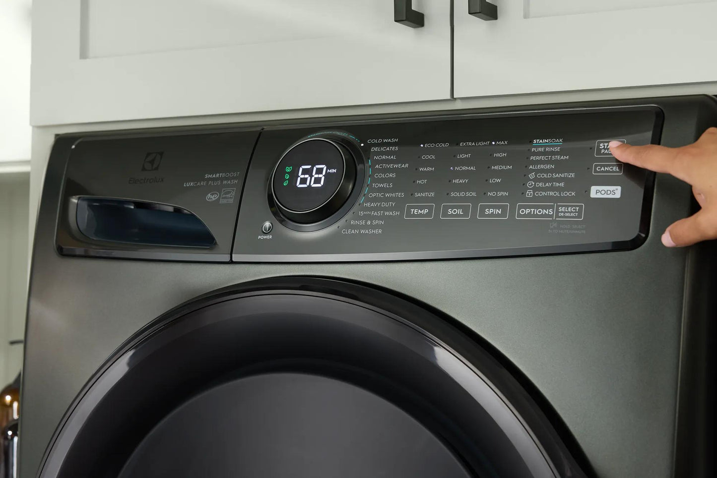Close-up of dark gray front load washer control panel showing digital cycle timer and hand pressing start button