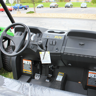 Dashboard and steering wheel area of a green John Deere crossover utility vehicle showing control levers and pedals