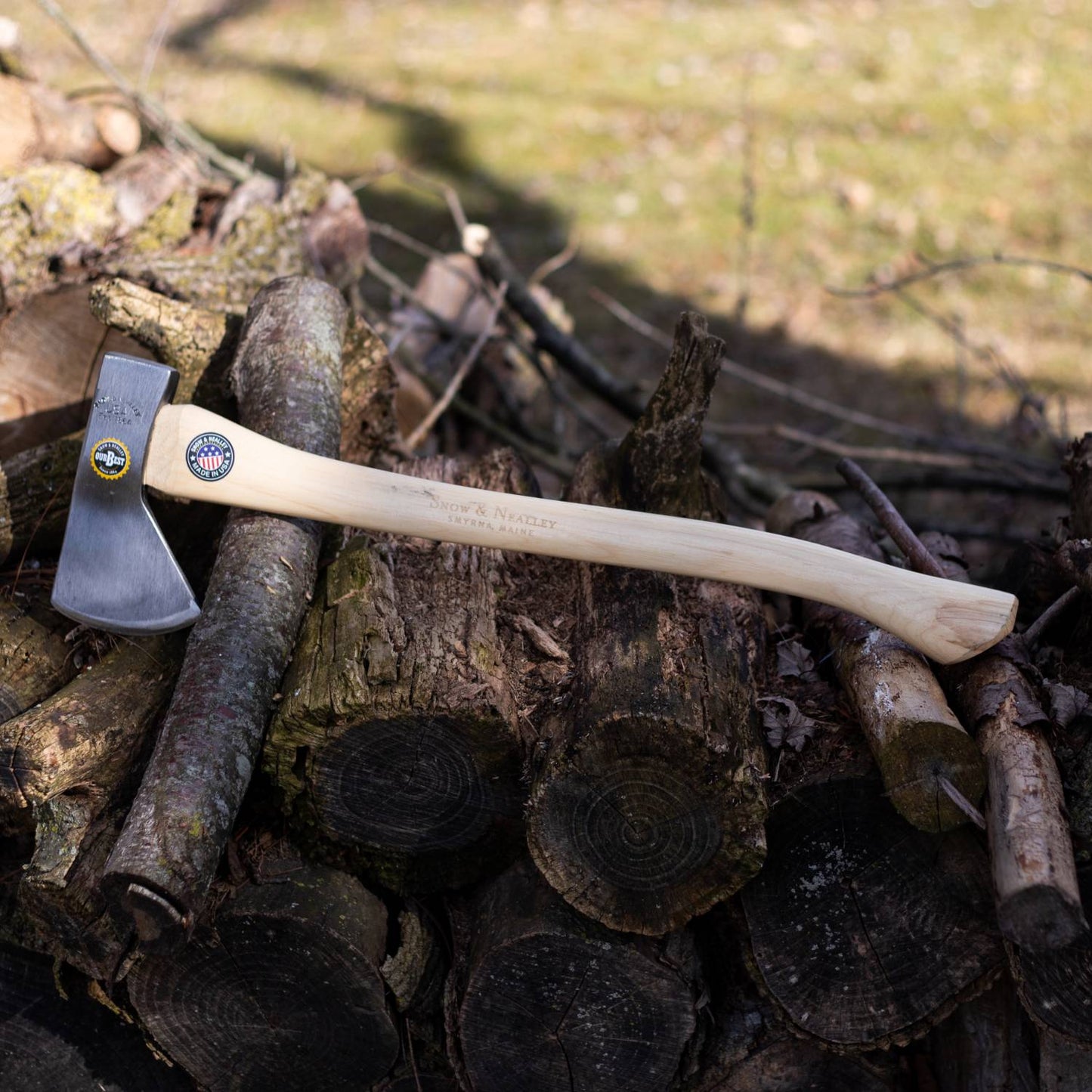 Camping axe with natural wooden handle and sharp steel head resting on a pile of cut firewood for tool accessories use