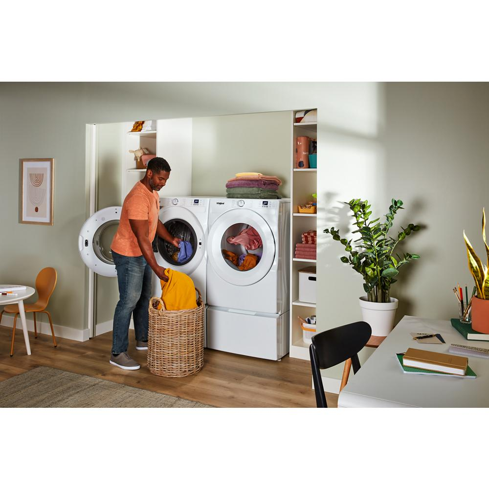 Man loading yellow clothes into white front load washer and dryer set in organized laundry area with woven basket and shelving