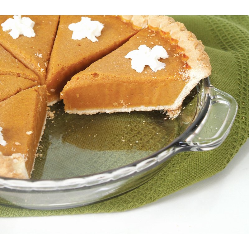 Clear glass pie plate holding sliced pumpkin pie with dollops of whipped cream on a green kitchen towel under $50 bakeware collection