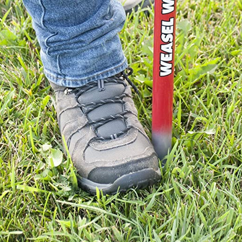 Person pressing red-handled weed popper into green grass for weed removal in home improvement tasks