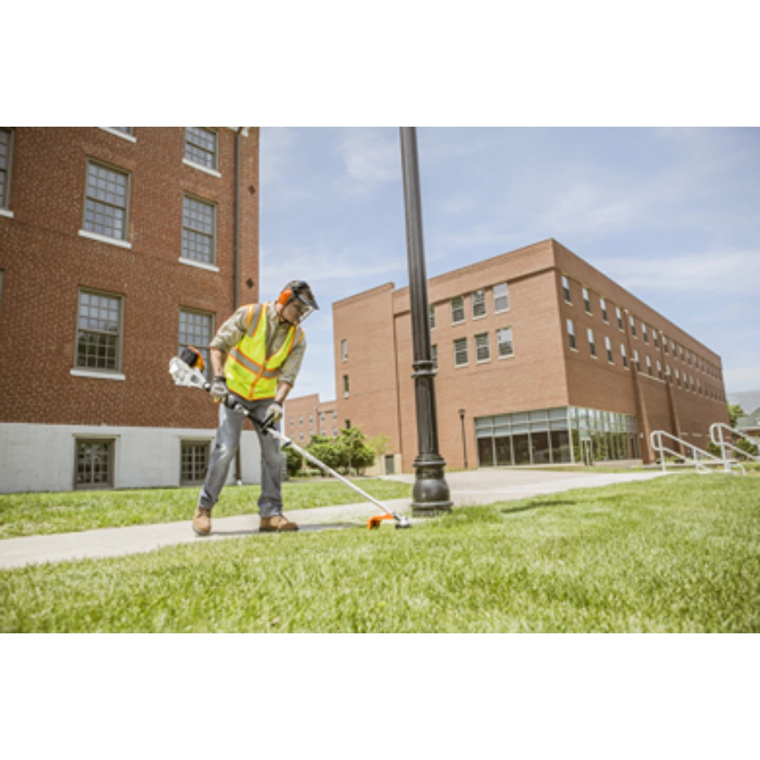 Person wearing safety gear using a STIHL KM 111 R KombiMotor for precise grass trimming near a sidewalk and lamp post