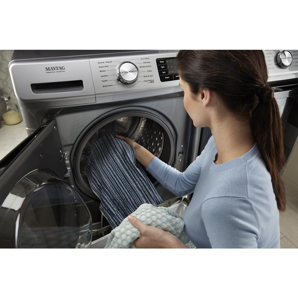 Woman loading striped and patterned garments into a front load gas dryer with Extra Power control in home appliance setting