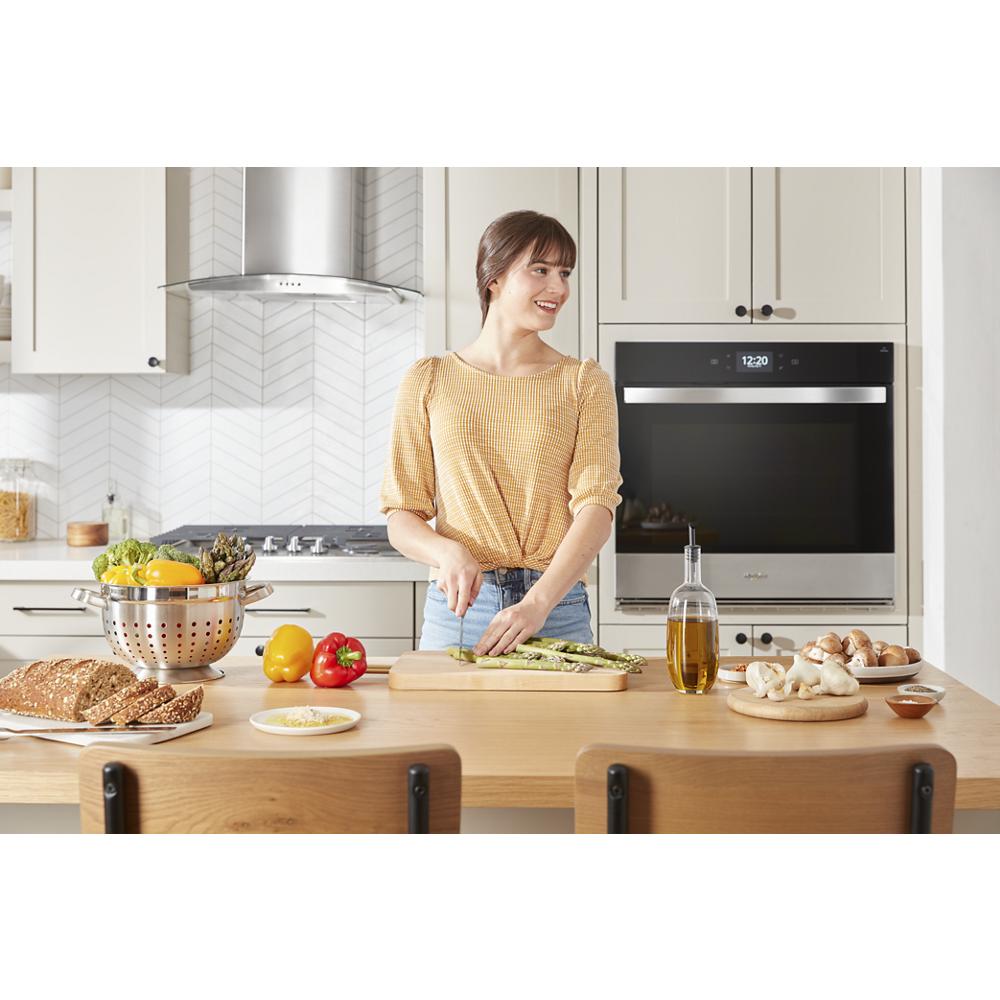 Woman preparing vegetables in kitchen with stainless steel wall oven microwave combo and modern appliances
