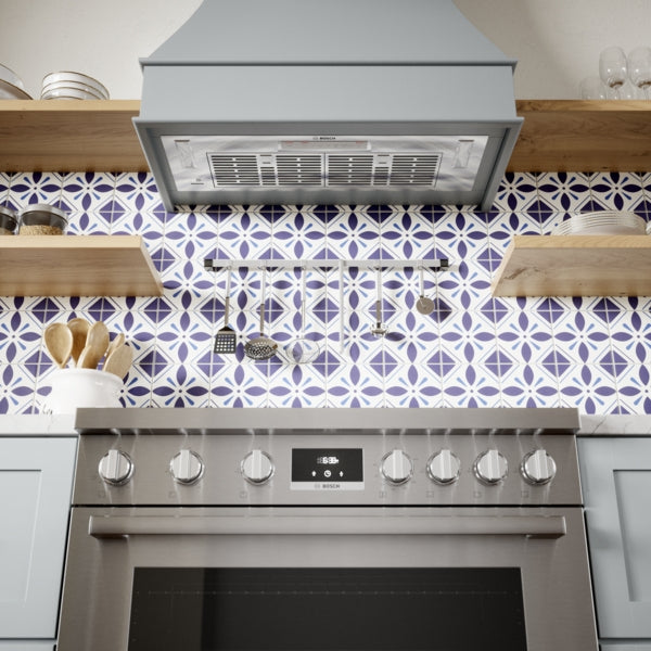 Stainless steel range hood insert with mesh filters and control panel above a modern stainless oven in kitchen appliances