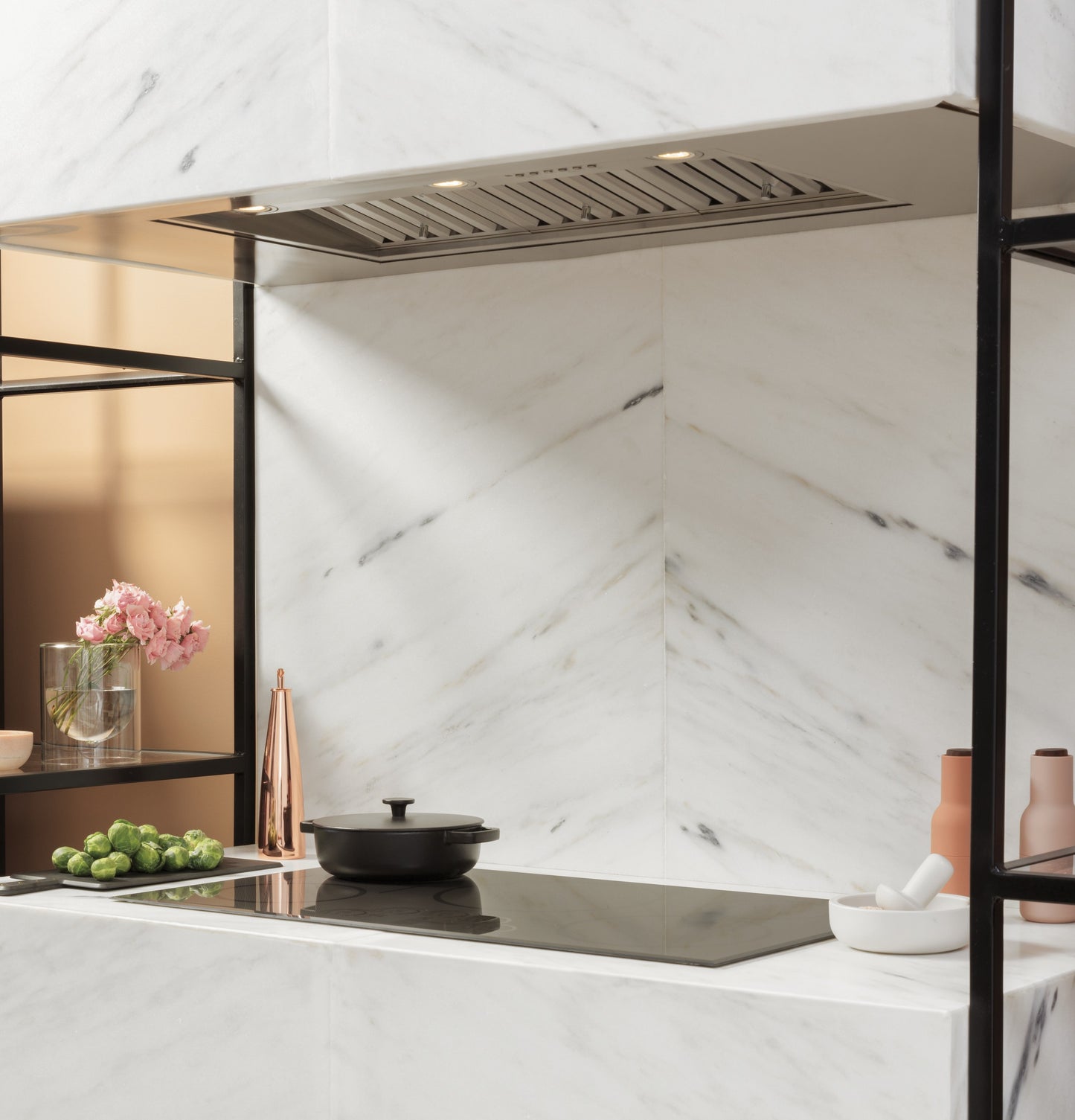 Marble kitchen corner with built-in cooktop, steel vent insert, decorative flowers, and modern kitchenware elements