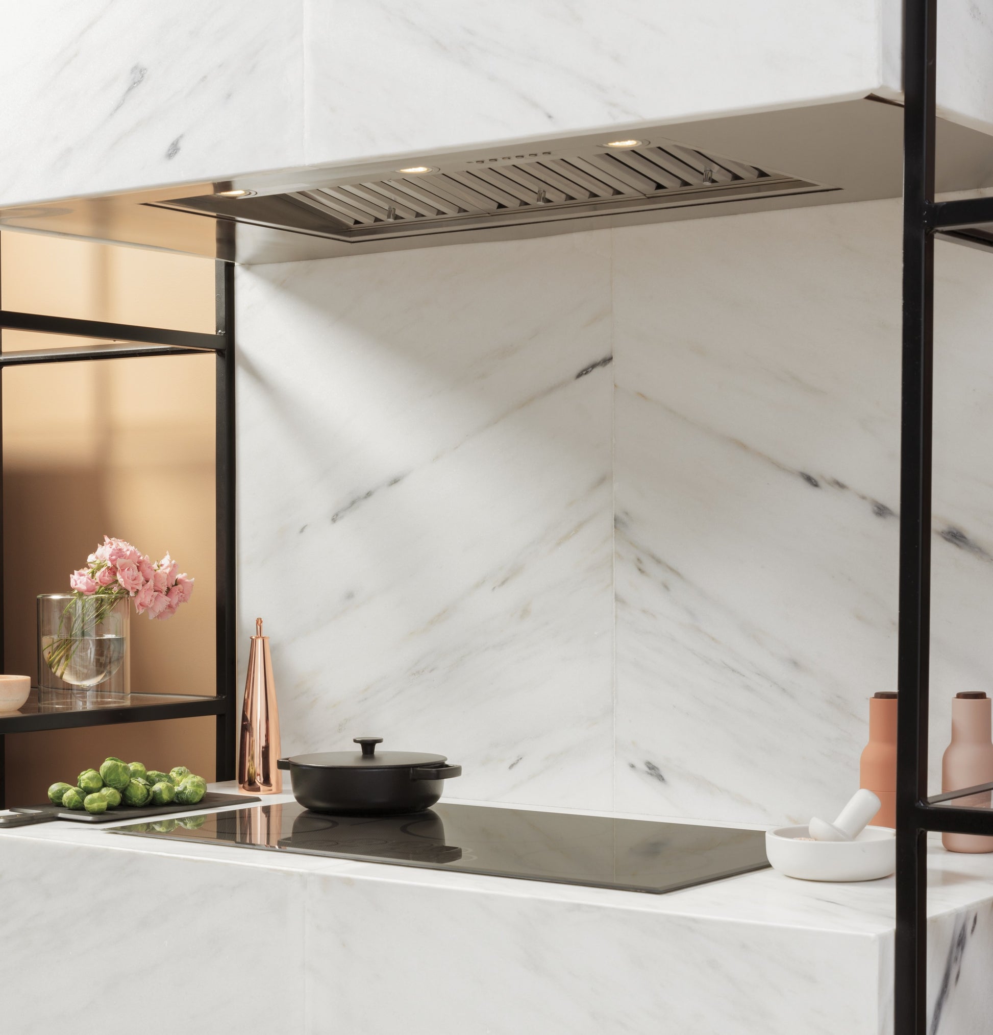 Marble kitchen corner with built-in cooktop, steel vent insert, decorative flowers, and modern kitchenware elements