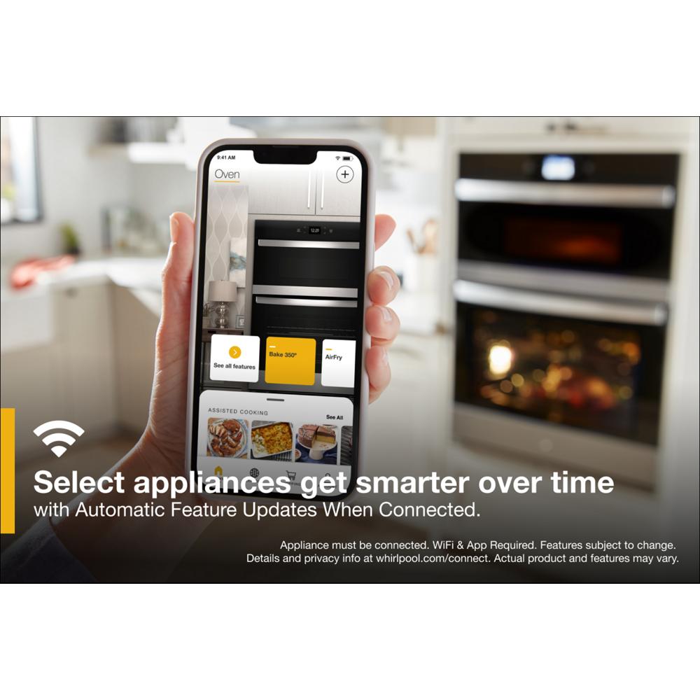 Hand holding smartphone displaying smart oven app in modern kitchen with wall oven microwave combo in background