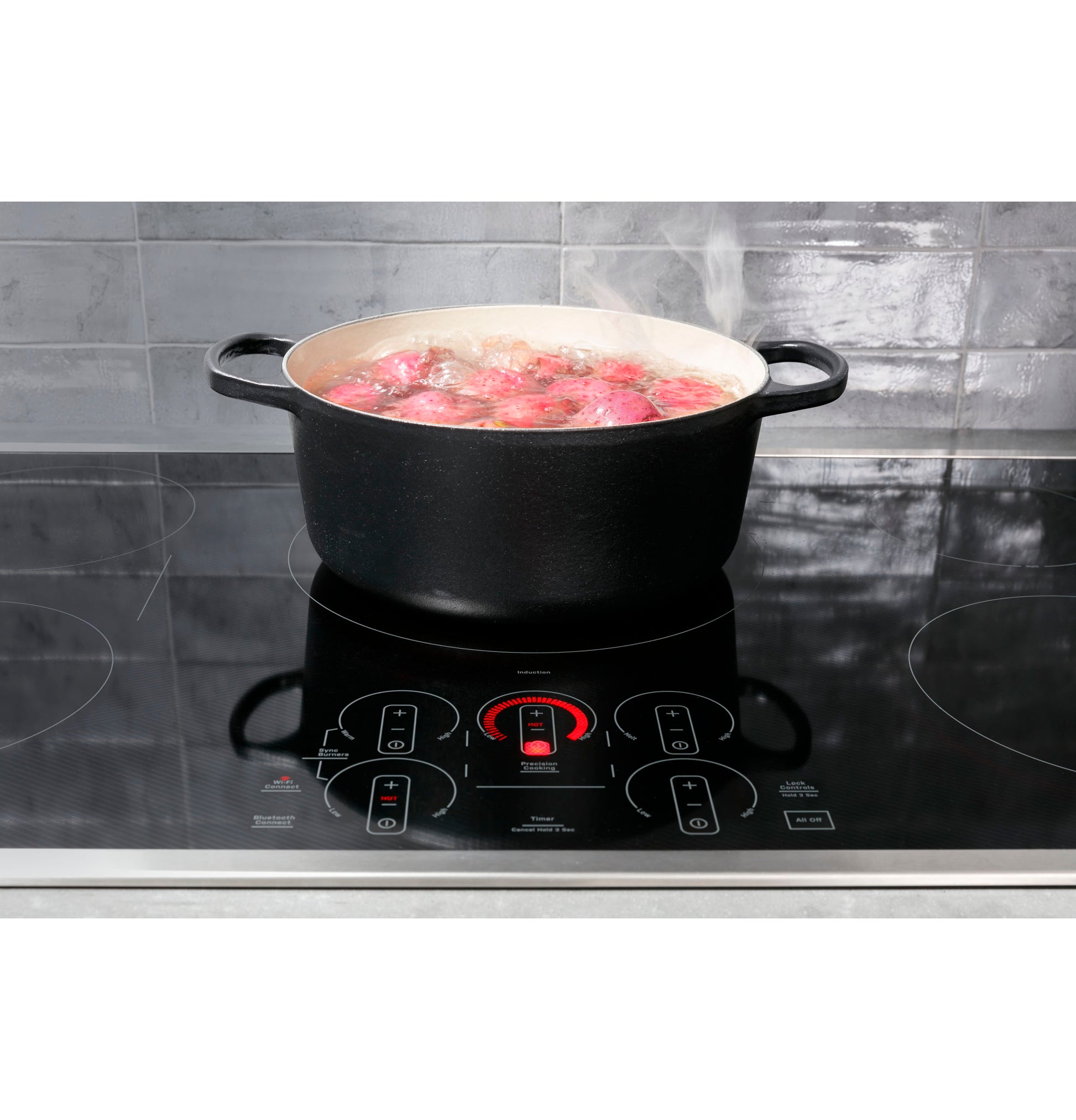 Black pot boiling water with red potatoes on touch control induction cooktop in modern kitchen setting