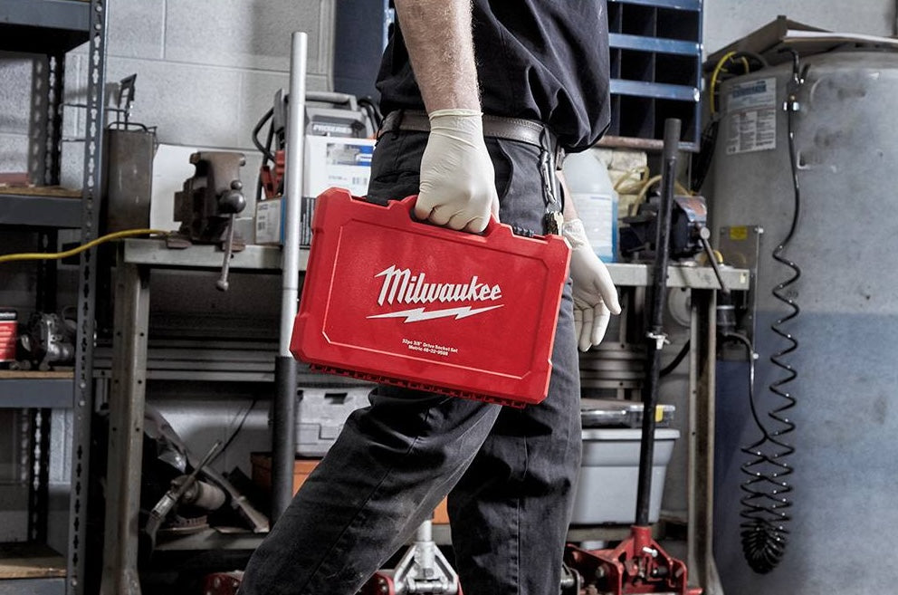 Person carrying a red Milwaukee steel case for hand tools in an industrial workshop setting
