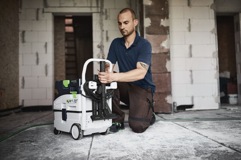 Person attaching a white and black handle accessory to a compact dust extractor in a woodworking environment