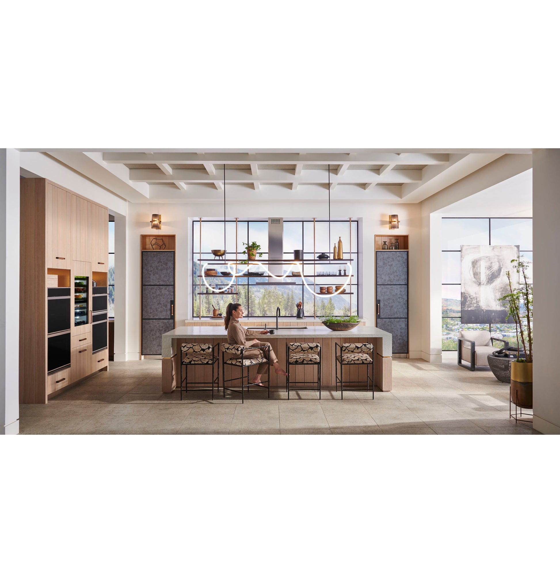 Elegant kitchen with Monogram minimalist double wall ovens installed in light wood cabinetry beside large island seating area and windows