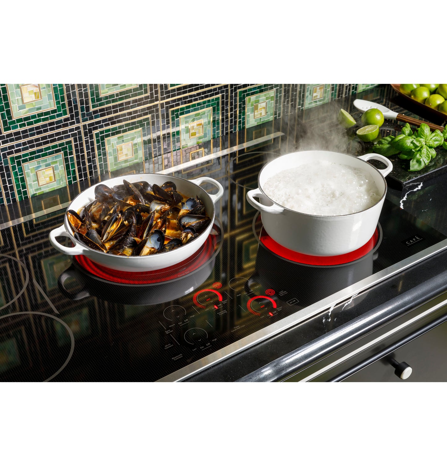 Glass electric cooktop with two white pots cooking mussels and boiling water in a modern kitchen setting