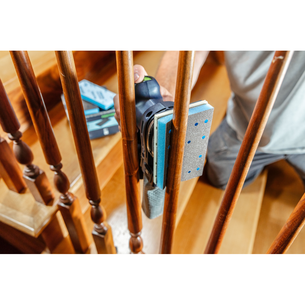 Person using power sander with blue abrasive pad on wooden stair railing in home improvement and tool accessories setting