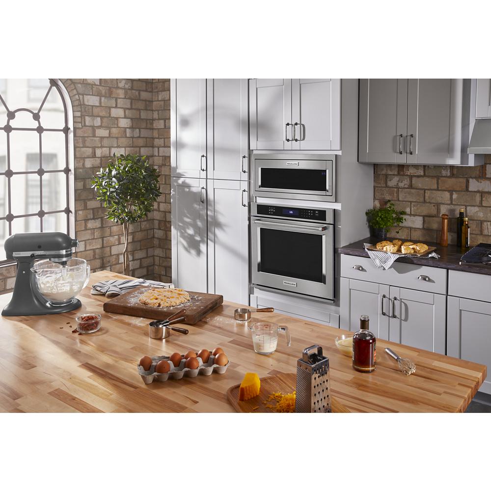 Modern kitchen with built-in stainless steel microwave and oven combo surrounded by white cabinetry and wood countertop workspace