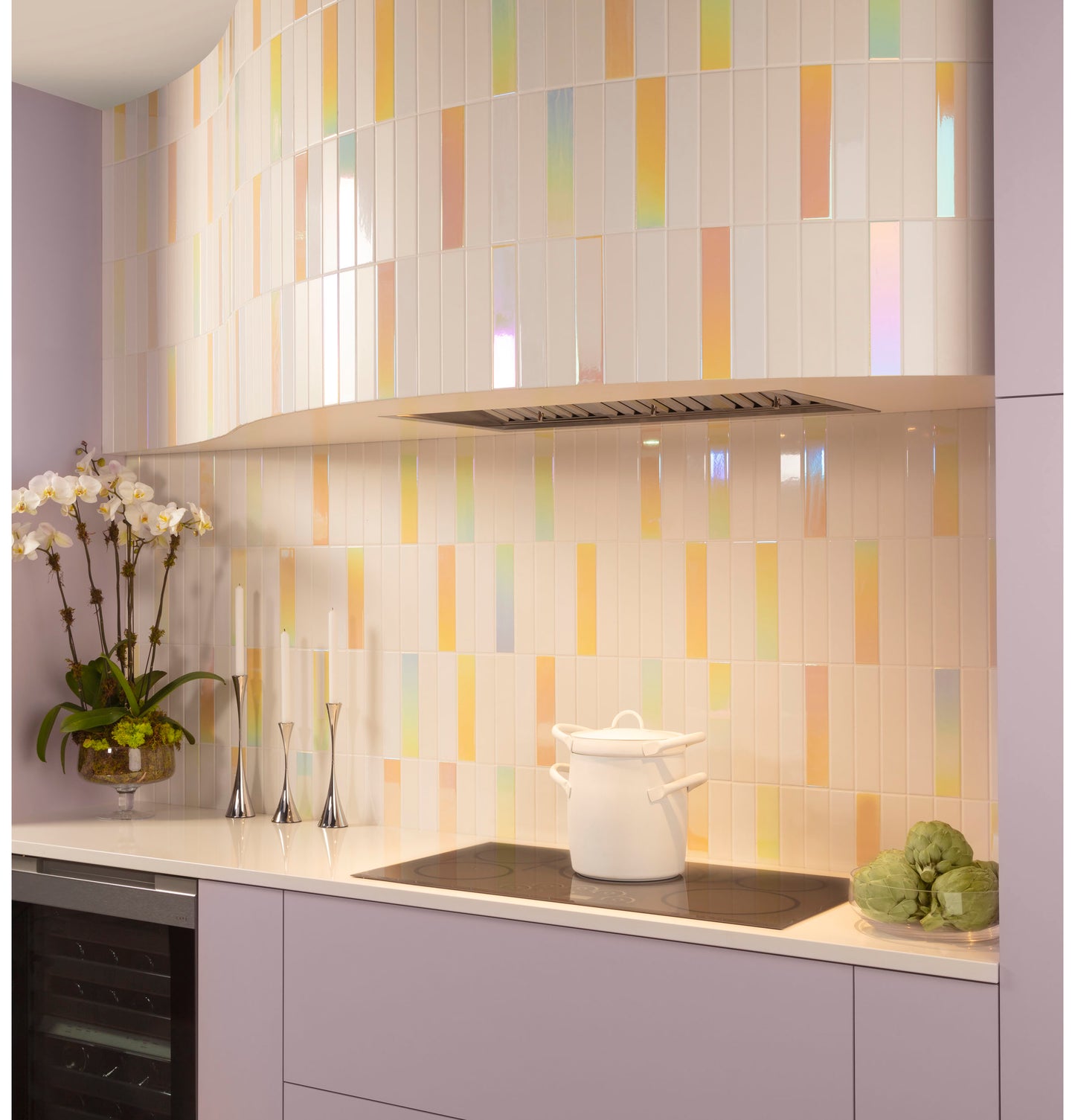 Kitchen cooktop area with pastel iridescent tile backsplash, lavender cabinetry, white countertop, and decorative plants