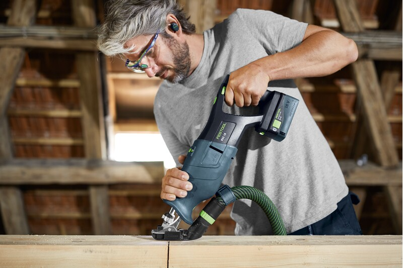 Man using cordless Festool power tool with dust extraction hose cutting wood in workshop setting