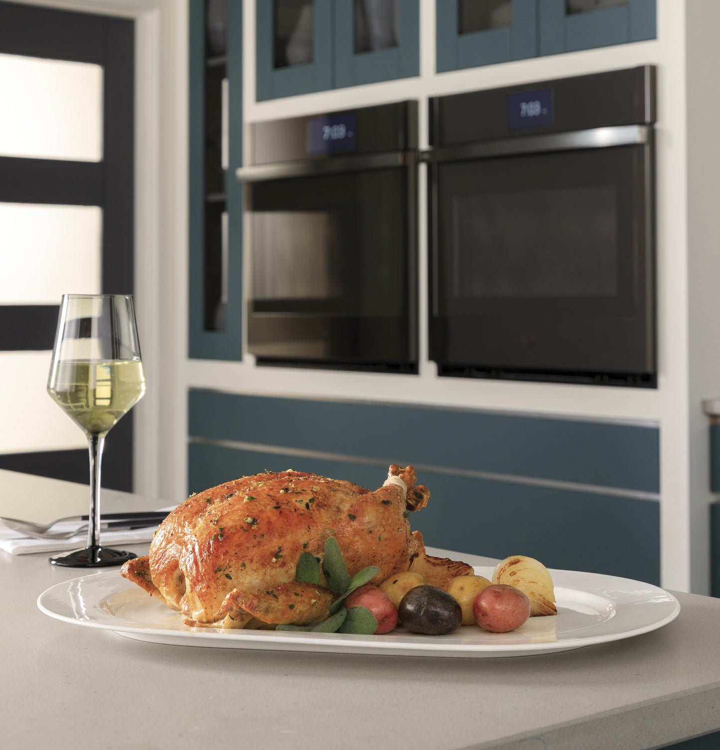 Roast chicken with vegetables plated on kitchen island in front of built-in double wall ovens in modern kitchen