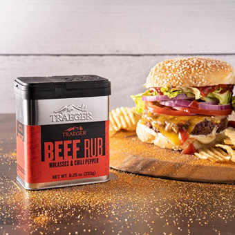 Metal container of Traeger molasses and chili pepper beef rub next to a cheeseburger with lettuce and tomato