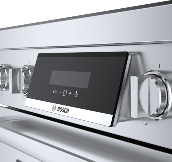 Close-up of stainless steel induction range control panel with ergonomic tilted black display and heavy-duty metal knobs