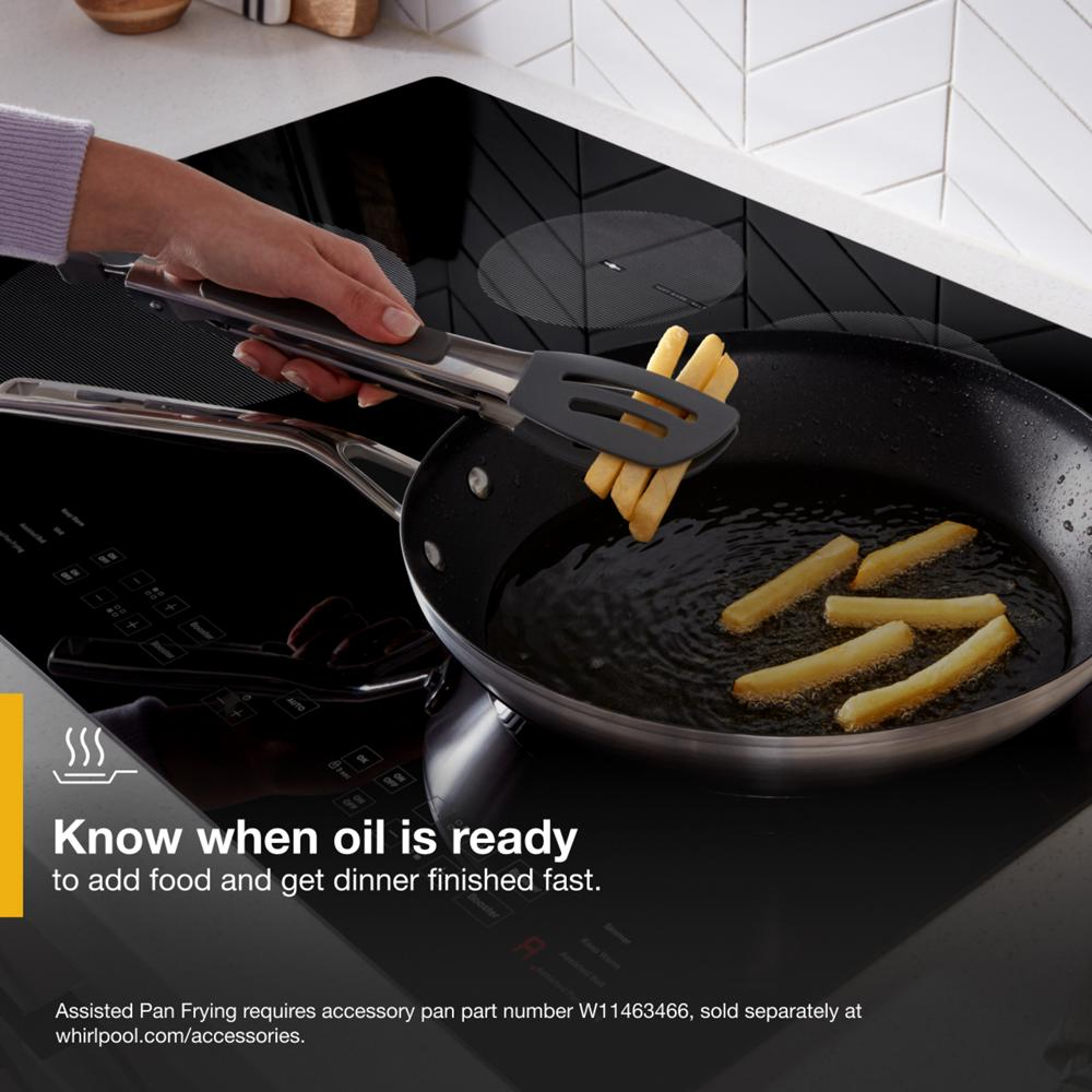 Hand using tongs to fry fries in black pan on sleek black 30-inch induction cooktop in modern kitchen setting