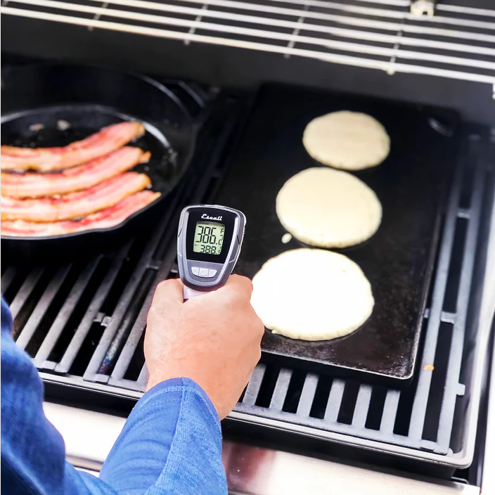 Handheld infrared thermometer measuring temperature on griddle with pancakes and bacon in kitchen gadgets collection