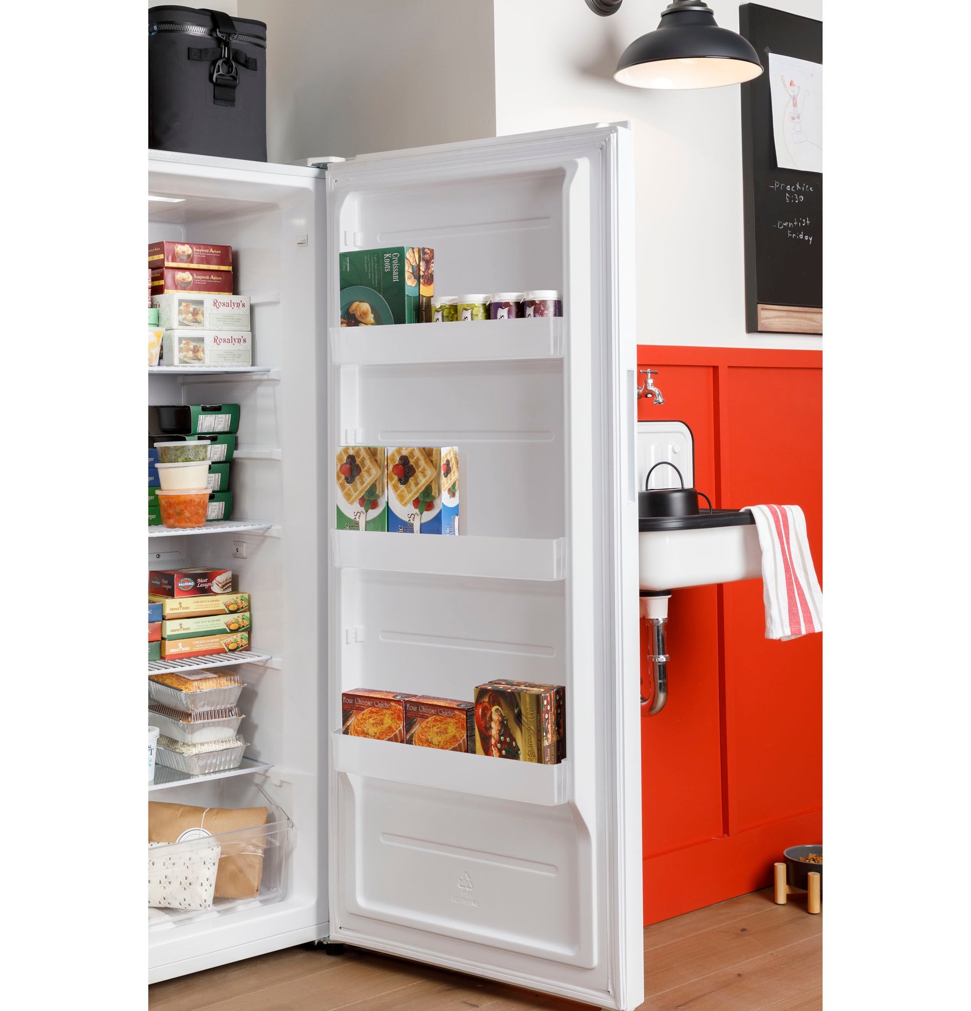 Open upright freezer door revealing organized frozen food and clear storage bins in a bright kitchen setting
