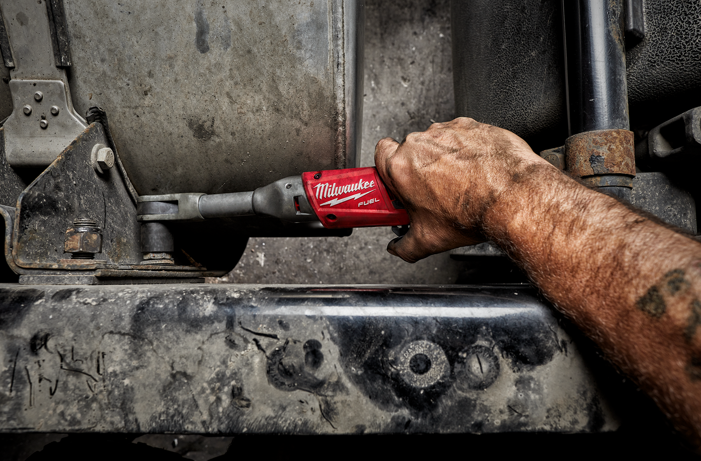 Hand gripping red Milwaukee cordless extended reach ratchet tightening bolt on metal machinery for repairs