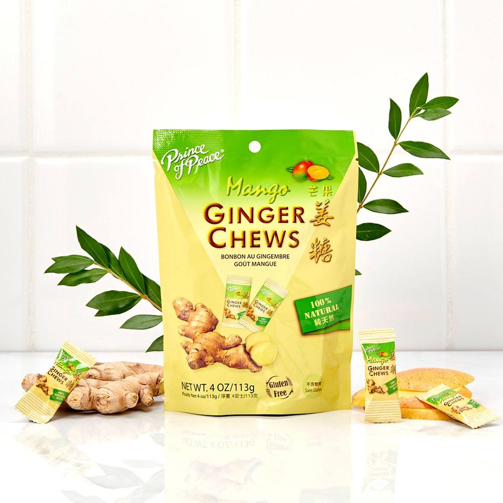 Green and yellow package of mango ginger chews with fresh ginger root and leaves on white surface