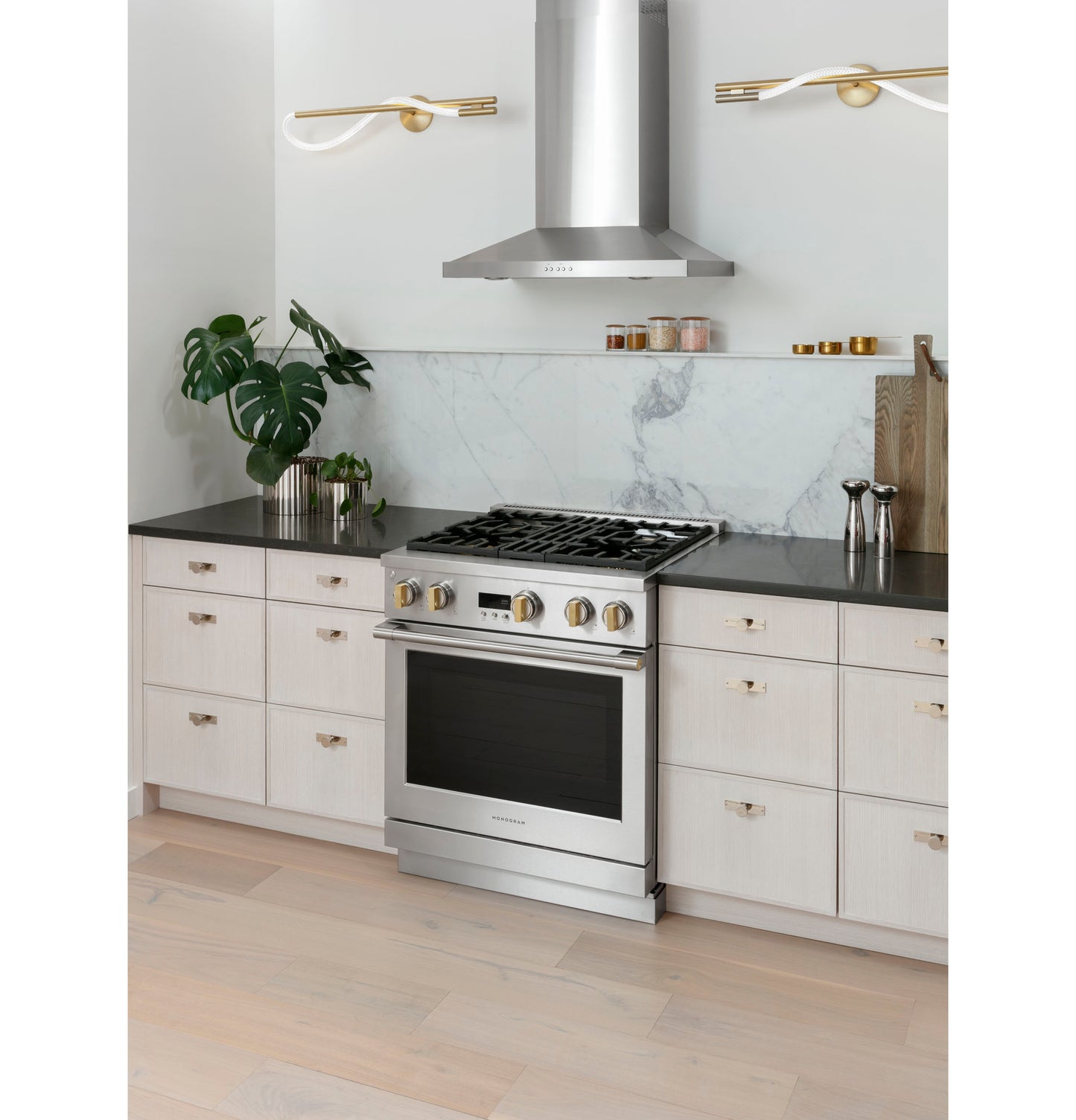 Sleek stainless steel wall-mounted vent hood above gas range with marble backsplash in modern kitchen setting