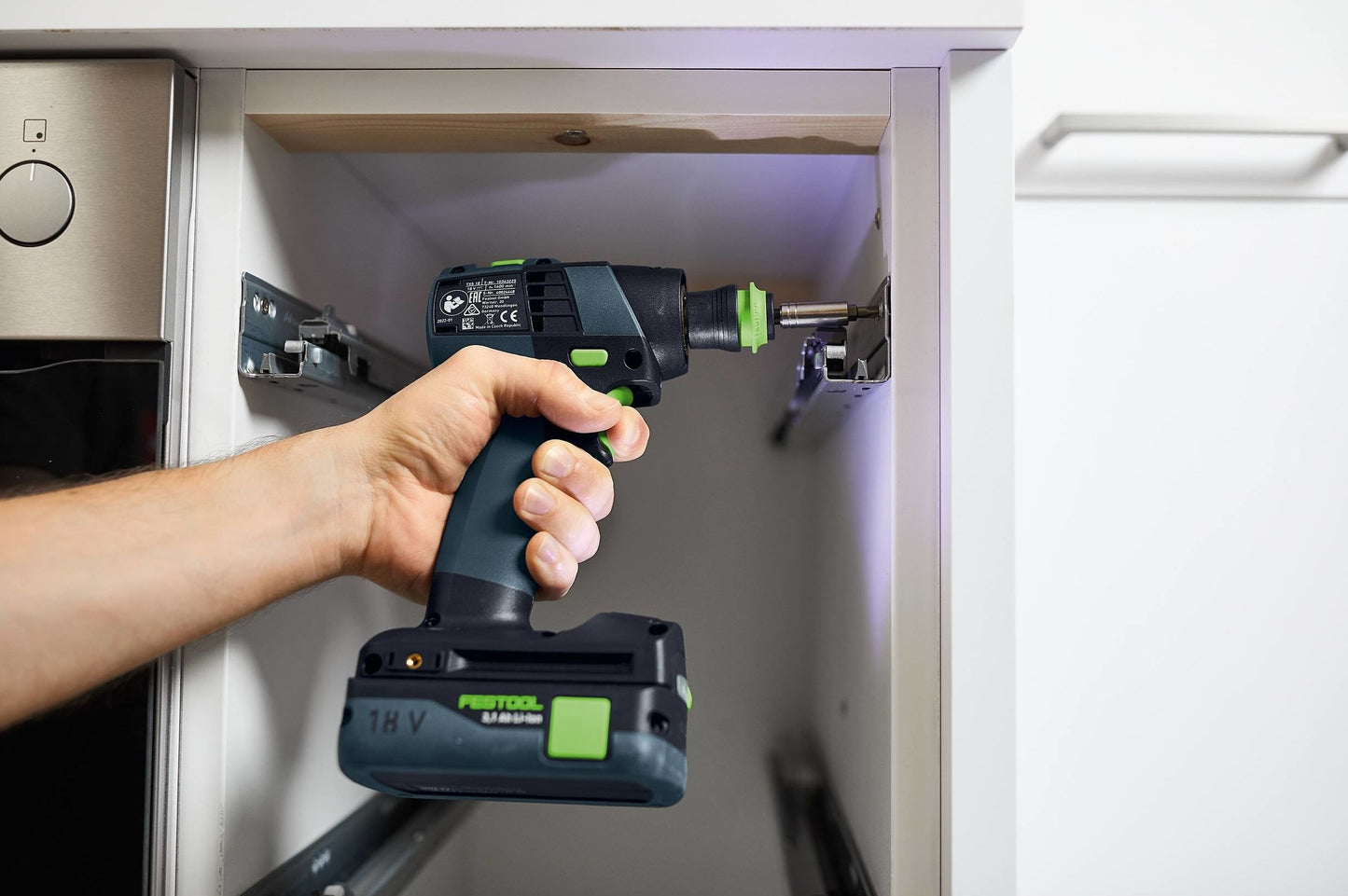 Person using a compact Festool cordless drill to install hardware inside a white cabinet for woodworking tasks