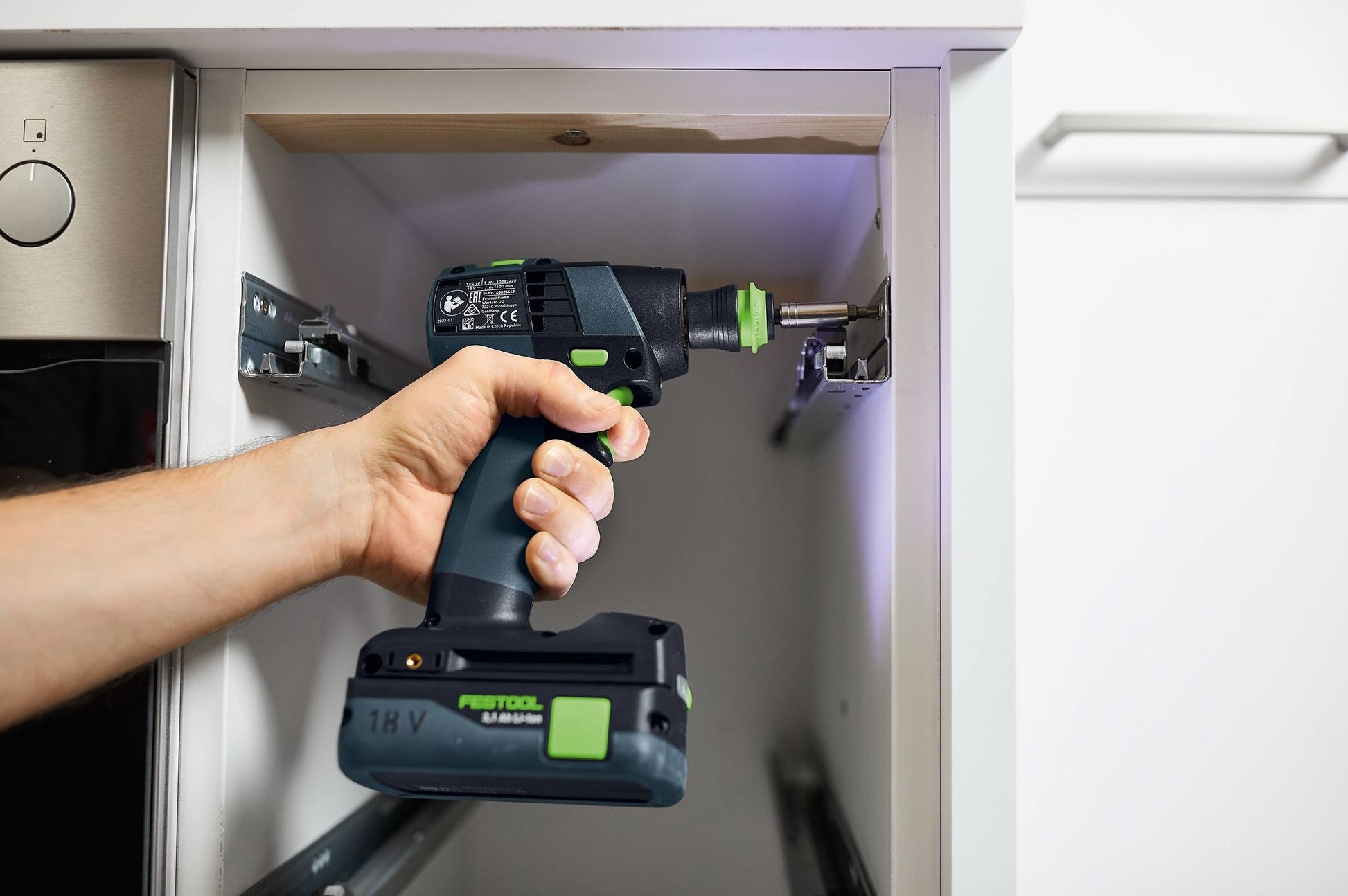 Person using a compact Festool cordless drill to install hardware inside a white cabinet for woodworking tasks