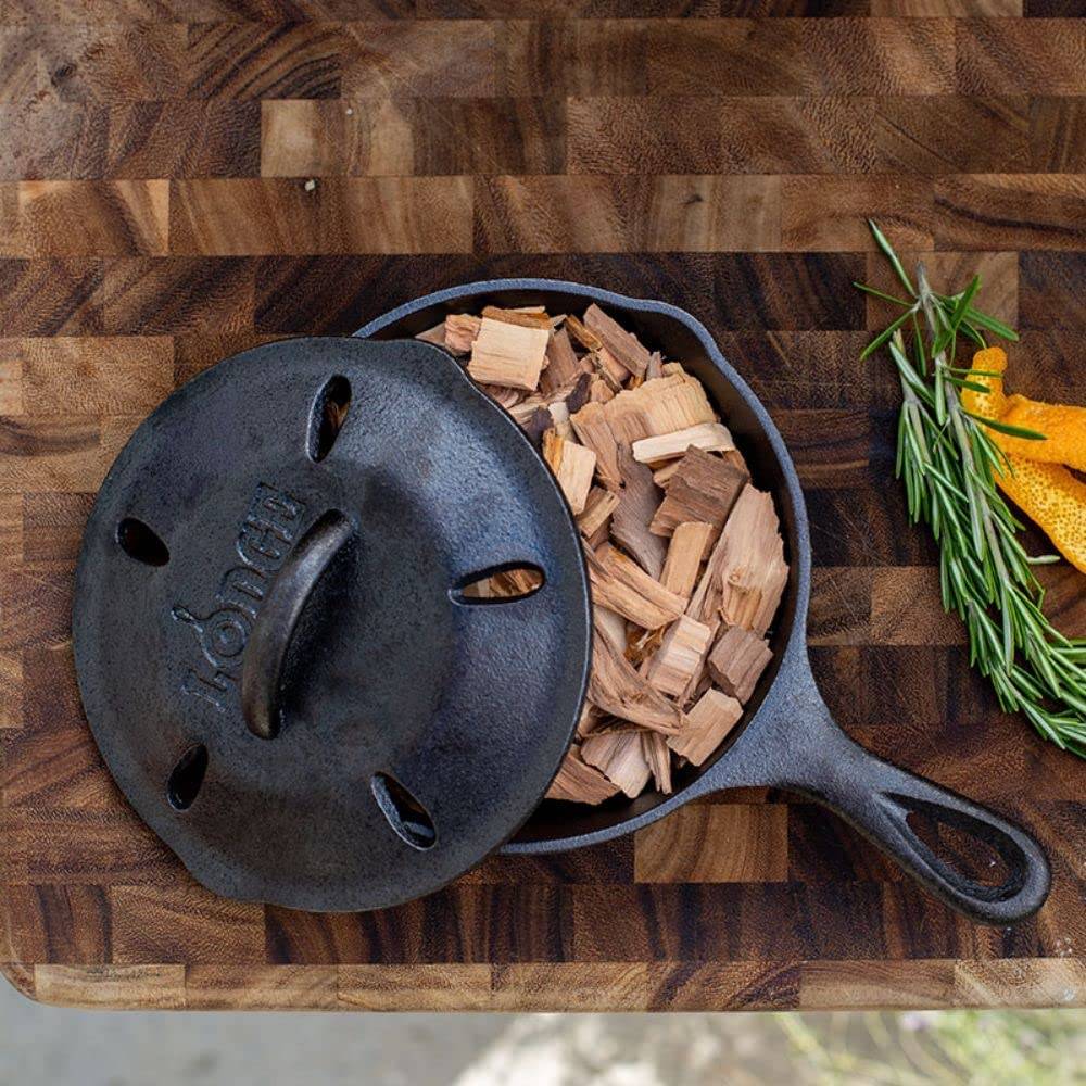 6.5-inch cast iron smoker skillet with lid and wood chips on butcher block in kitchenware collections