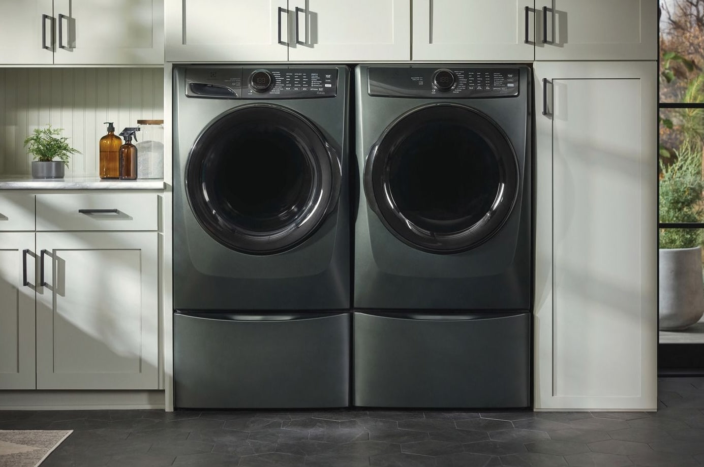 Modern laundry setup featuring two dark front-load appliances elevated on matching pedestals with storage in a stylish laundry room