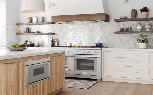 Built-in stainless steel microwave drawer integrated into modern wooden kitchen island with light cabinetry and open shelving