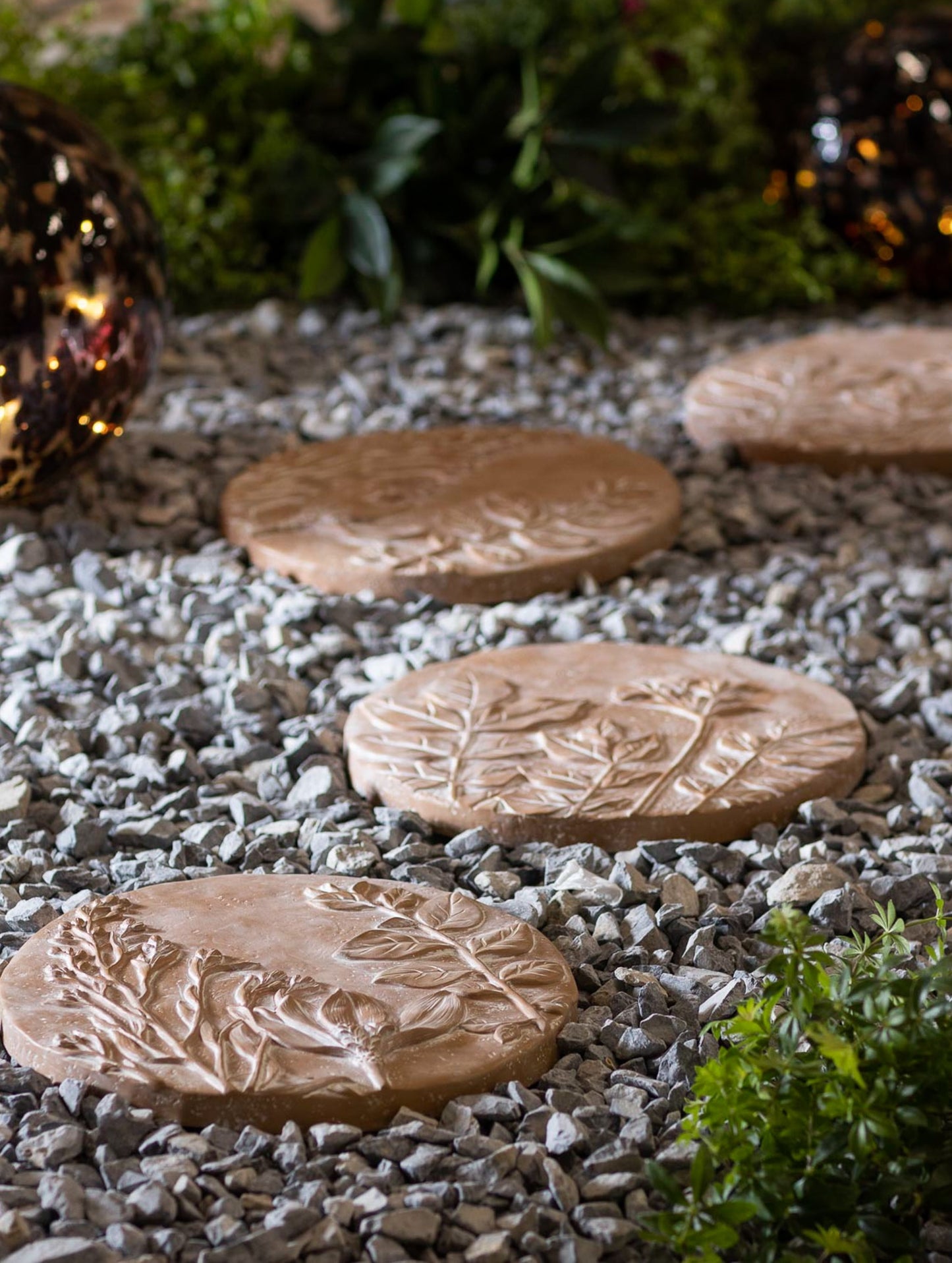 Round terracotta stepping stones with raised floral and leaf designs set on gray gravel for garden paths and home improvement